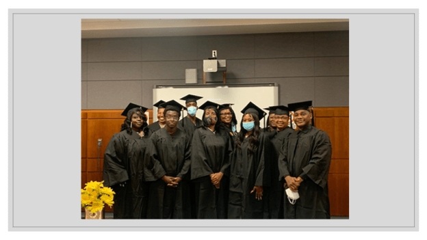 A group of graduates wearing gowns, hats, and some in masks, smiling together