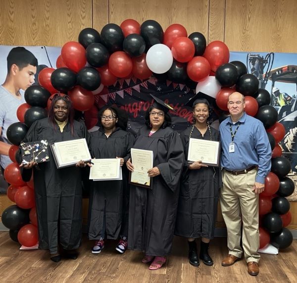 Group of graduates holding their diplomas, and a faculty member standing with balloons and school images behind them.