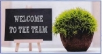 Sign with welcome to the team written on it next to a plant.