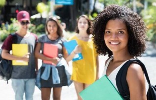 A girl smiling in the foreground with three other students smiling, in the background.